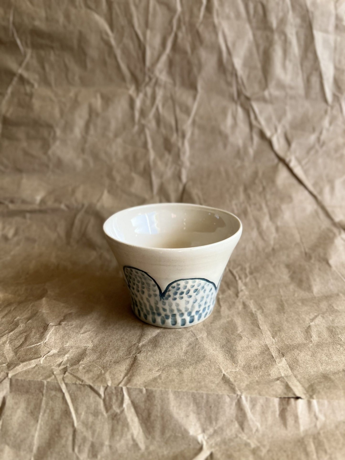 Handmade white ceramic cup with blue patterns on a crumpled brown paper background