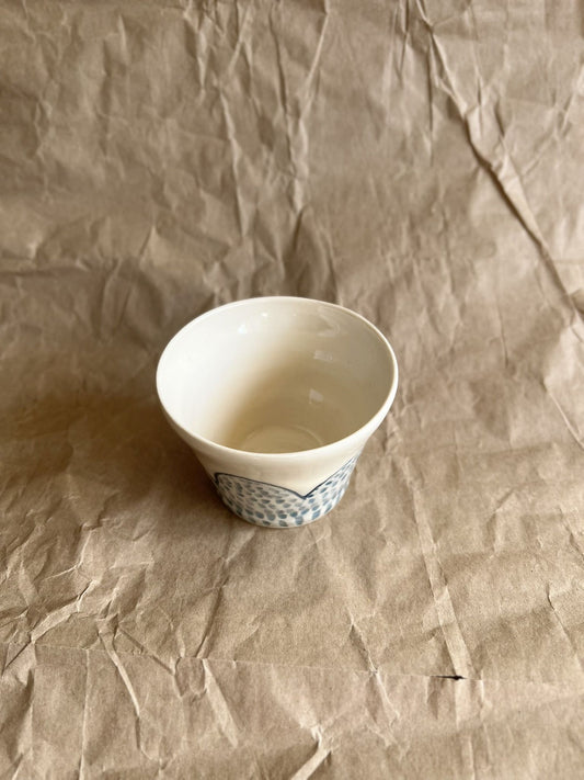Handmade white ceramic cup with blue patterns on a crumpled brown paper background