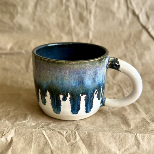Handmade ceramic mug with blue and white drippy glaze on a crumpled brown paper surface