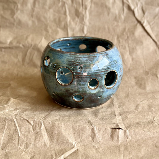 Blue ceramic votive with circular holes on a textured brown background