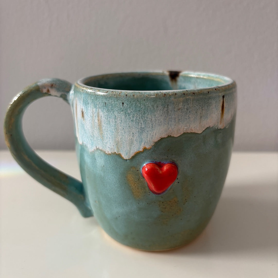 Blue ceramic mug with a sweet red heart on a white surface