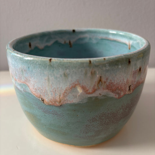 Turquoise blue ceramic bowl with speckled glaze rim on a light background