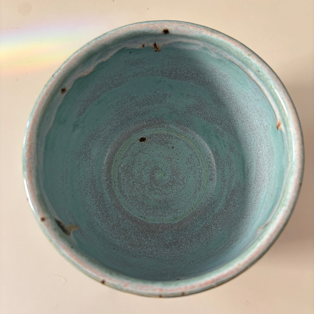 Turquoise blue ceramic bowl with speckled glaze rim on a light background