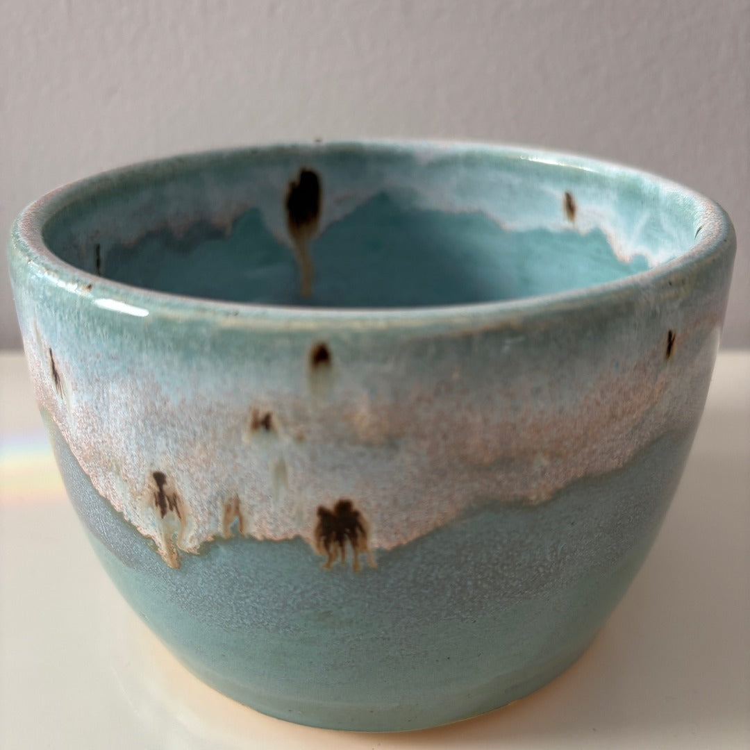 Turquoise blue ceramic bowl with speckled glaze rim on a light background
