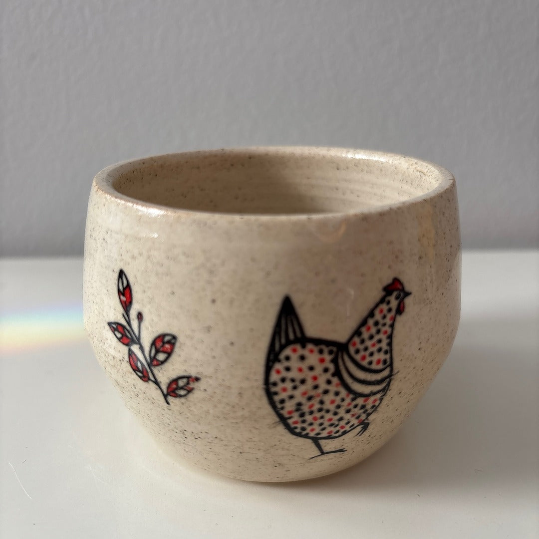 Ceramic white stoneware bowl with a black and red chicken design on a white surface