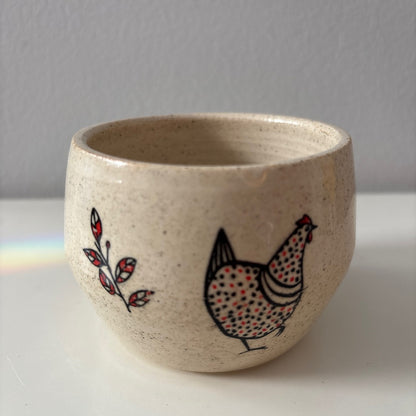 Ceramic white stoneware bowl with a black and red chicken design on a white surface