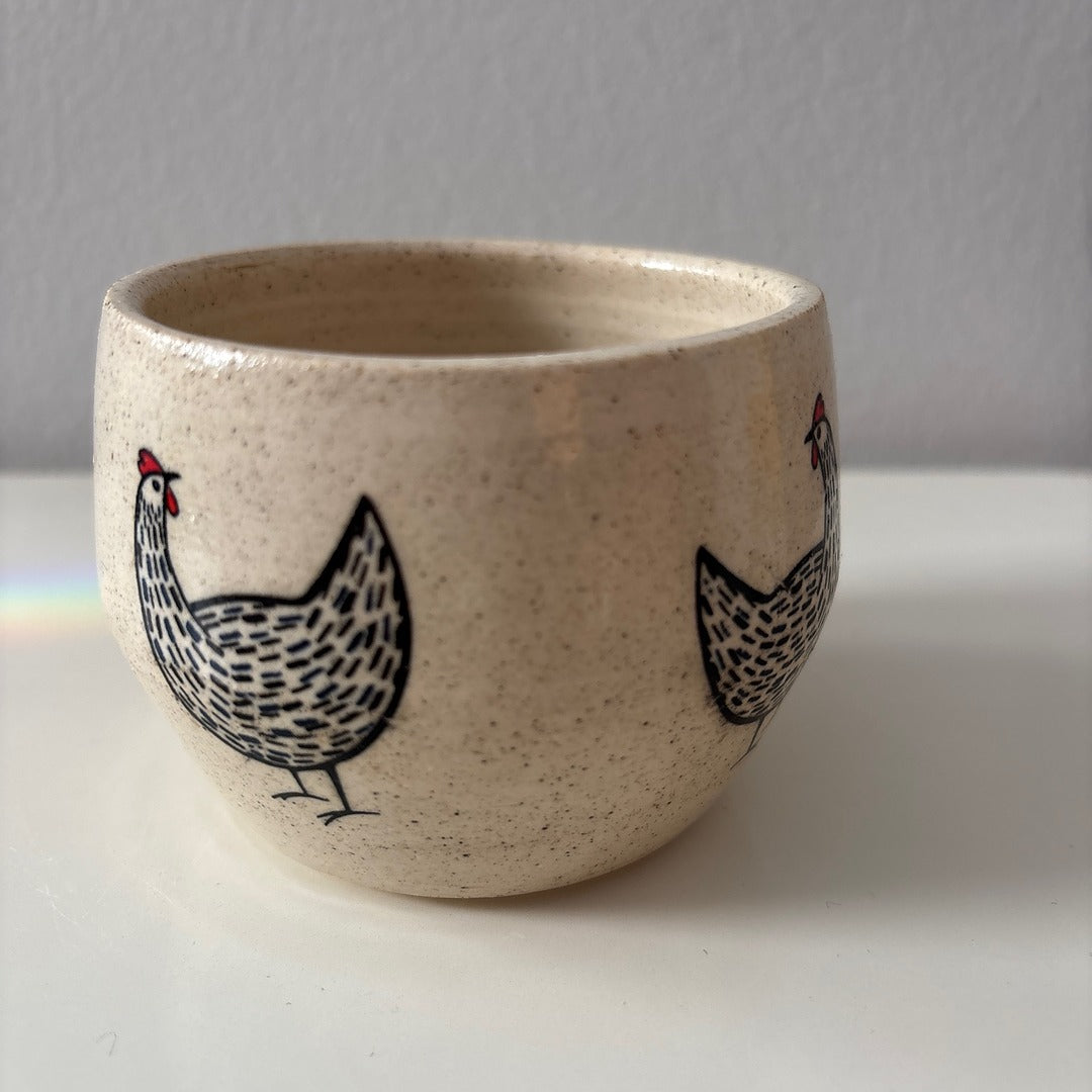 Ceramic white stoneware bowl with a black and red chicken design on a white surface
