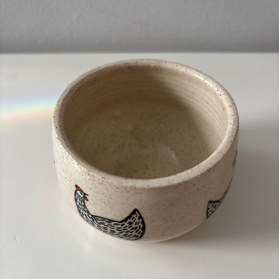 Ceramic white stoneware bowl with a black and red chicken design on a white surface