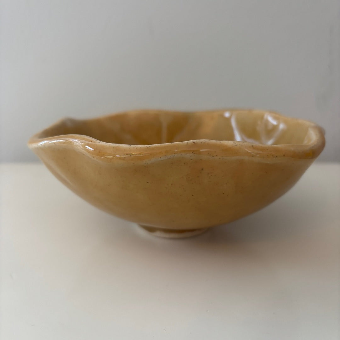 Honey colored scalloped ceramic bowl on a light background