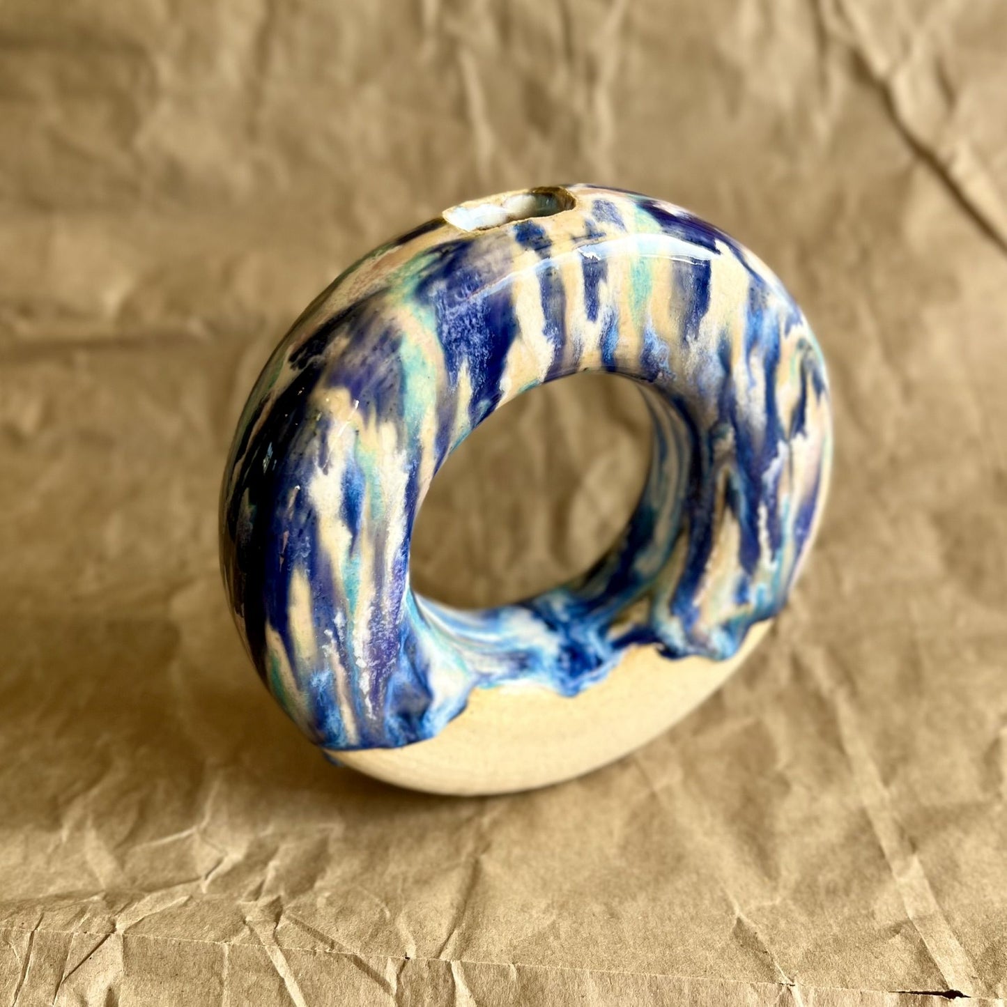 Ceramic donut vase with blue and white glaze on a crumpled brown paper background