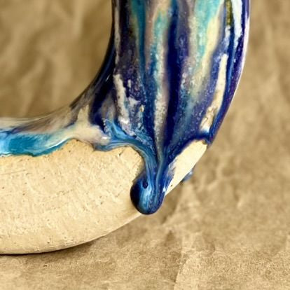 Handmade ceramic donut vase with blue and white glaze on a crumpled brown paper background