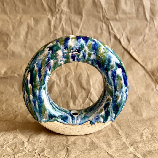 Handmade ceramic donut vase with blue and green glaze on a brown paper background