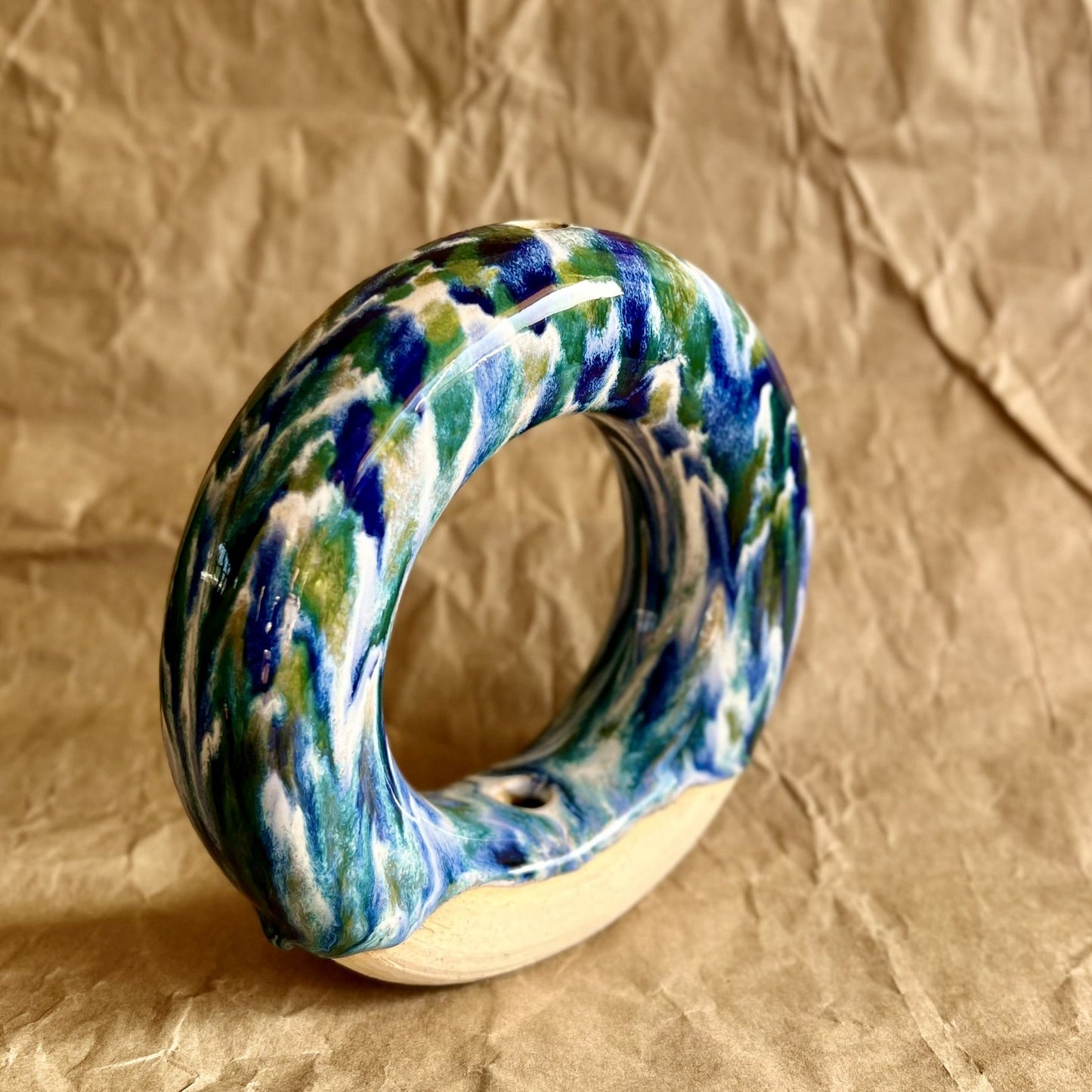 Handmade ceramic donut vase with blue and green glaze on a brown paper background
