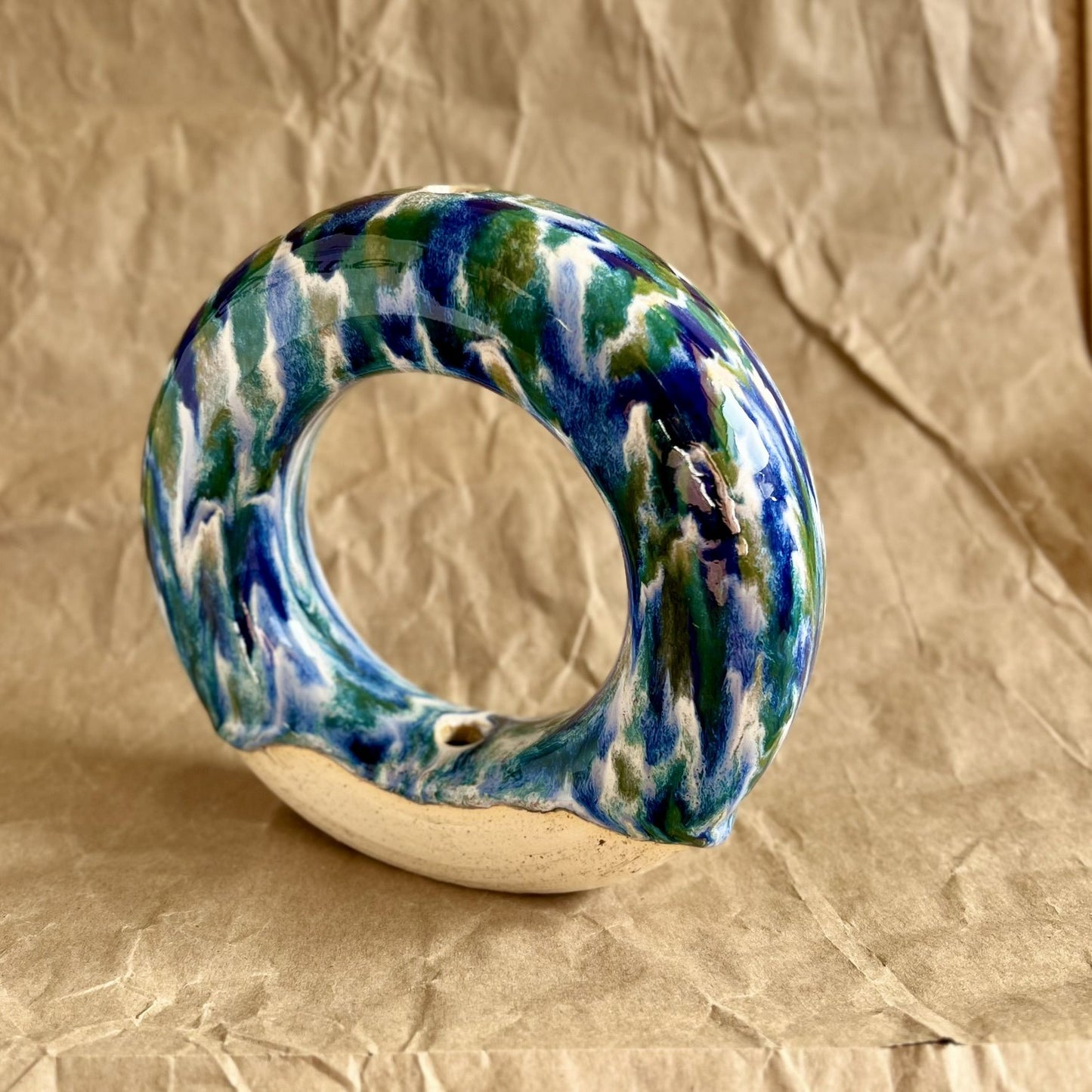 Handmade ceramic donut vase with blue and green glaze on a brown paper background