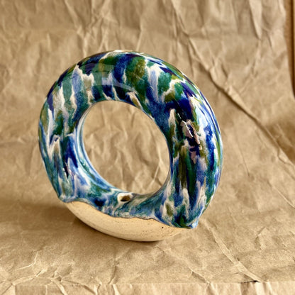 Handmade ceramic donut vase with blue and green glaze on a brown paper background