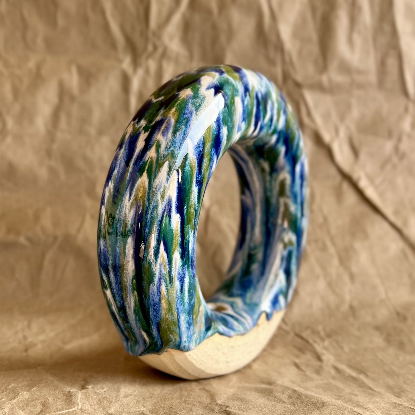 Handmade ceramic donut vase with blue and green glaze on a brown paper background