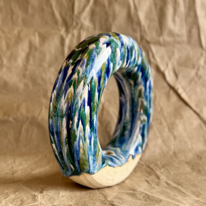 Handmade ceramic donut vase with blue and green glaze on a brown paper background