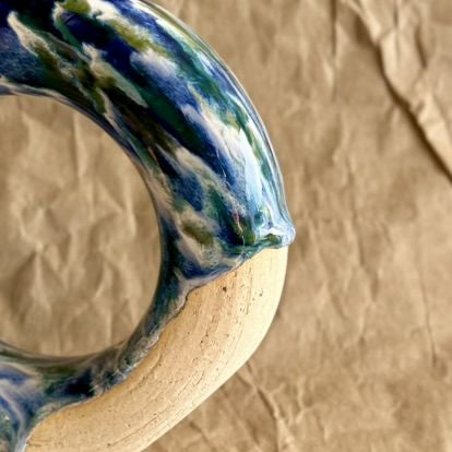 Handmade ceramic donut vase with blue and green glaze on a brown paper background