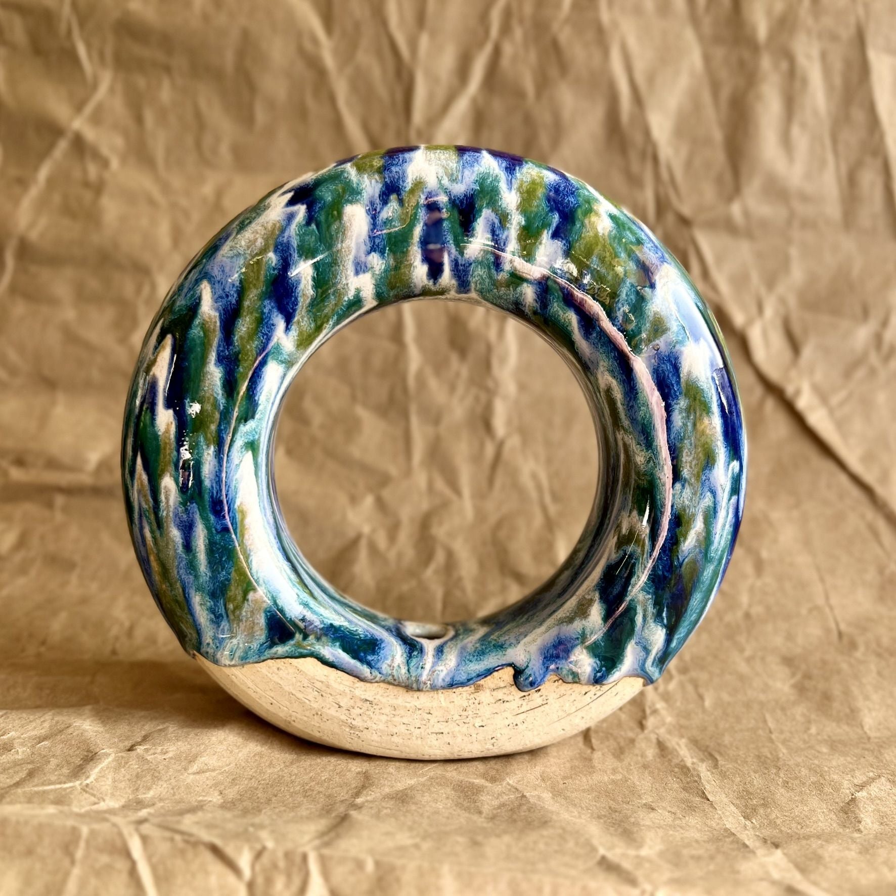 Handmade ceramic donut vase with blue and green glaze on a brown paper background