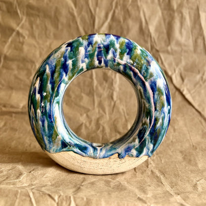 Handmade ceramic donut vase with blue and green glaze on a brown paper background