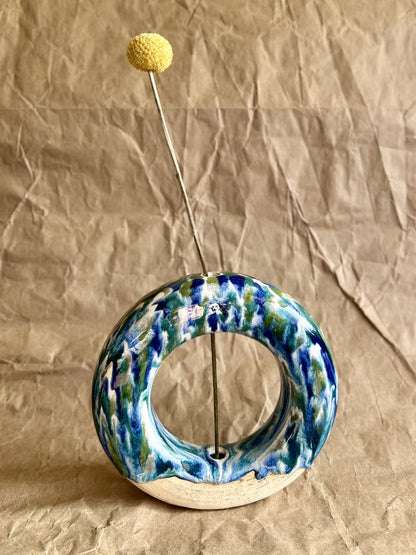 Handmade ceramic donut vase with yellow flower with blue and green glaze on a brown paper background