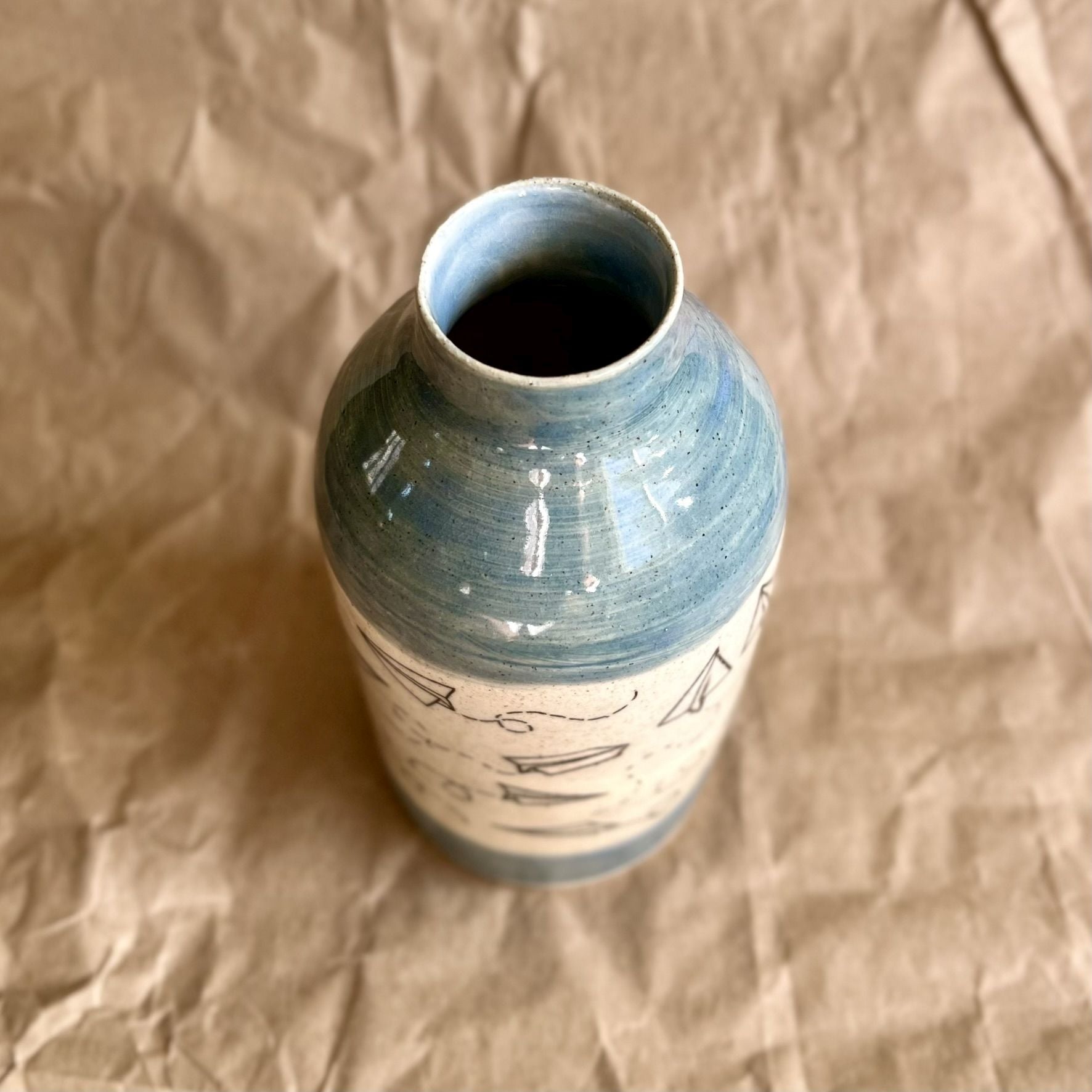 Ceramic vase with paper airplane design and blue accents on a brown textured background
