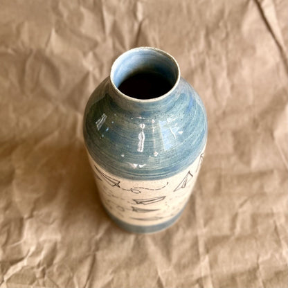 Ceramic vase with paper airplane design and blue accents on a brown textured background