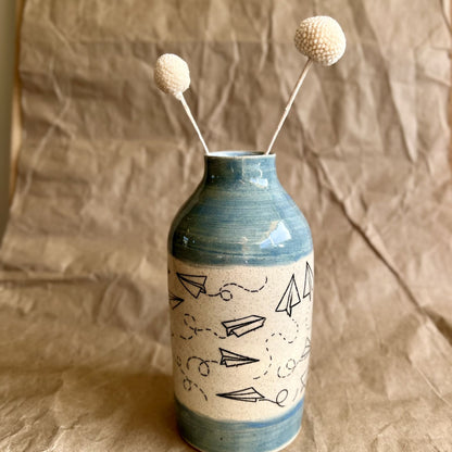 Ceramic vase with paper airplane design and blue accents on a brown textured background
