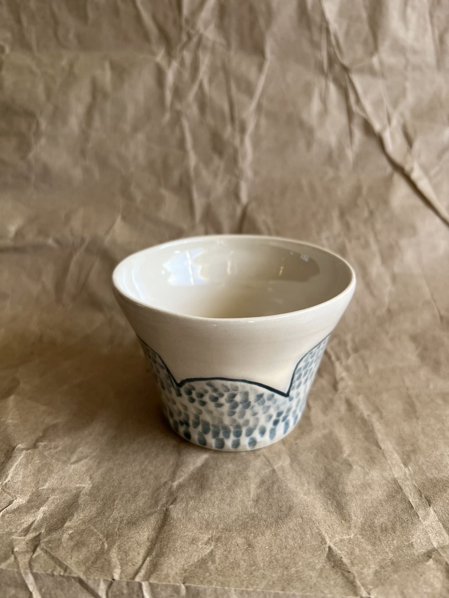 Handmade white ceramic cup with blue patterns on a crumpled brown paper background