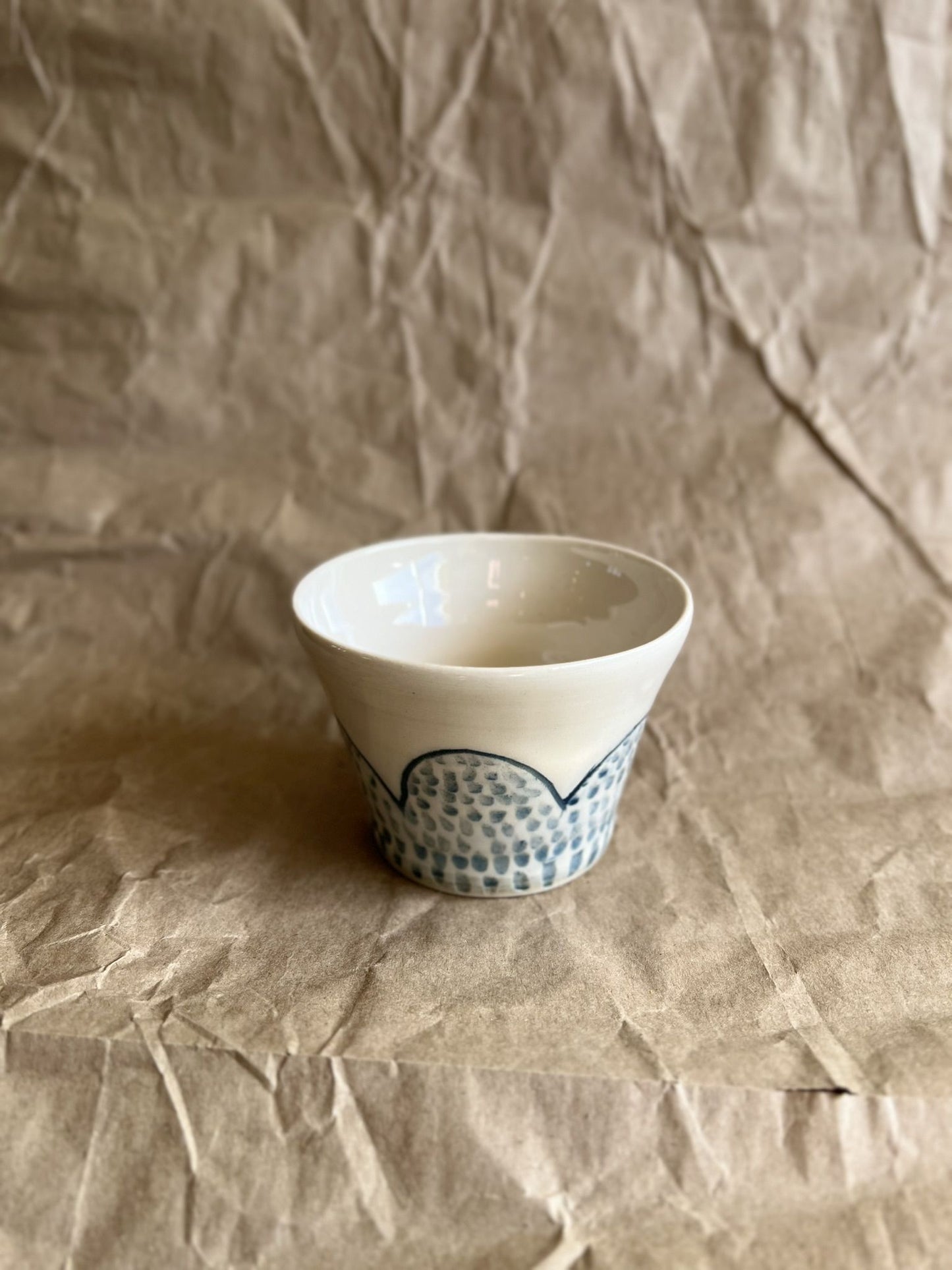 Handmade white ceramic cup with blue patterns on a crumpled brown paper background