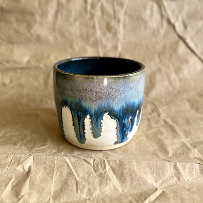 Handmade ceramic mug with blue and white drippy glaze on a crumpled brown paper surface
