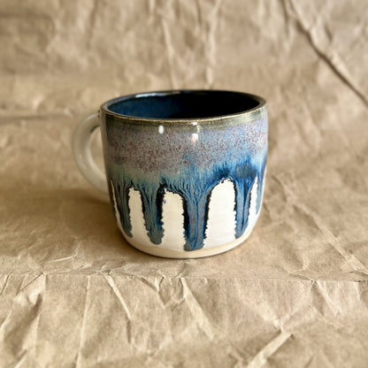 Handmade ceramic mug with blue and white drippy glaze on a crumpled brown paper surface
