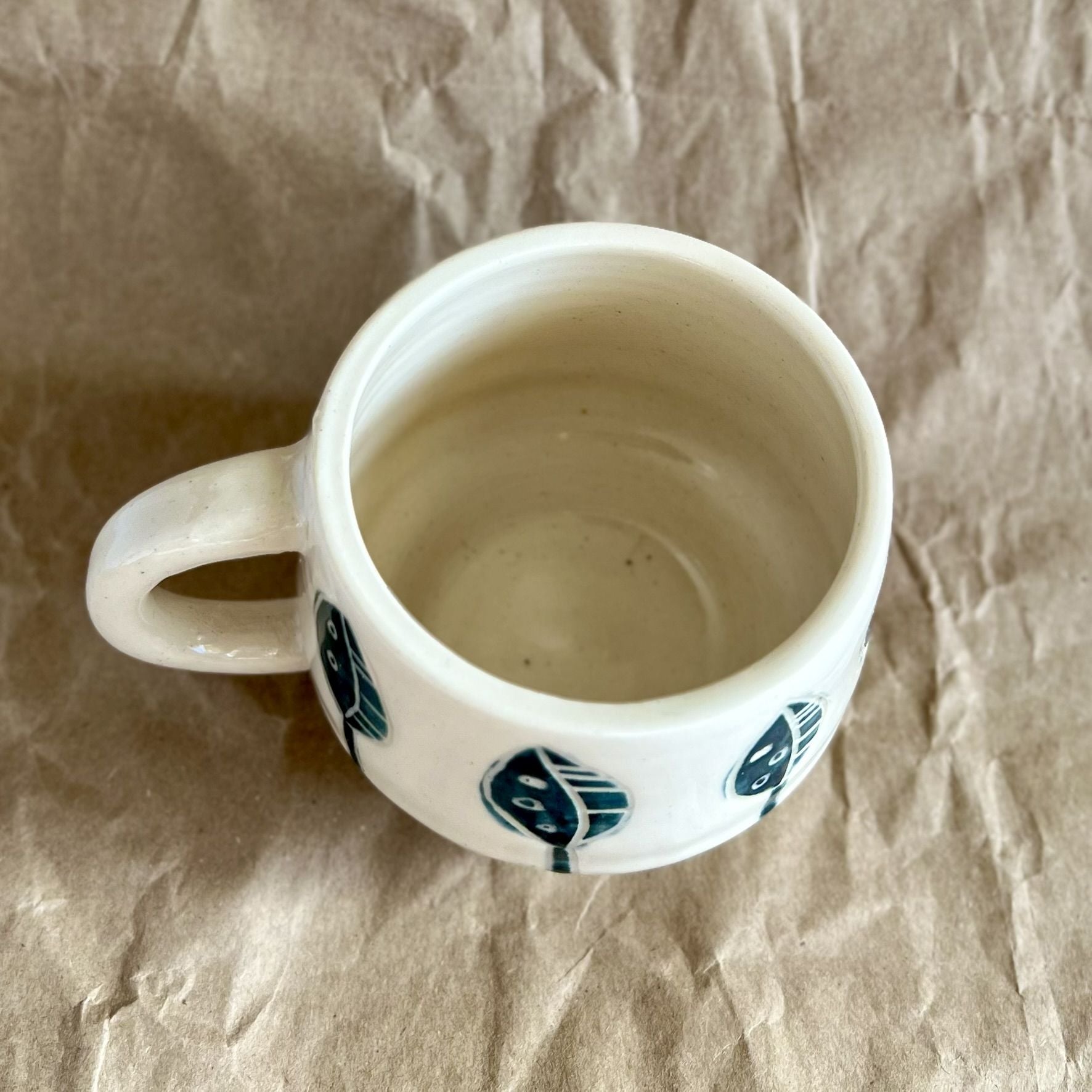 Handmade white ceramic mug with blue leaf designs on a textured brown surface