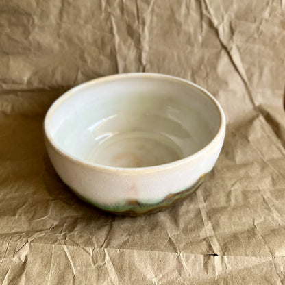 White ceramic bowl with green and walnut accent on a textured brown background