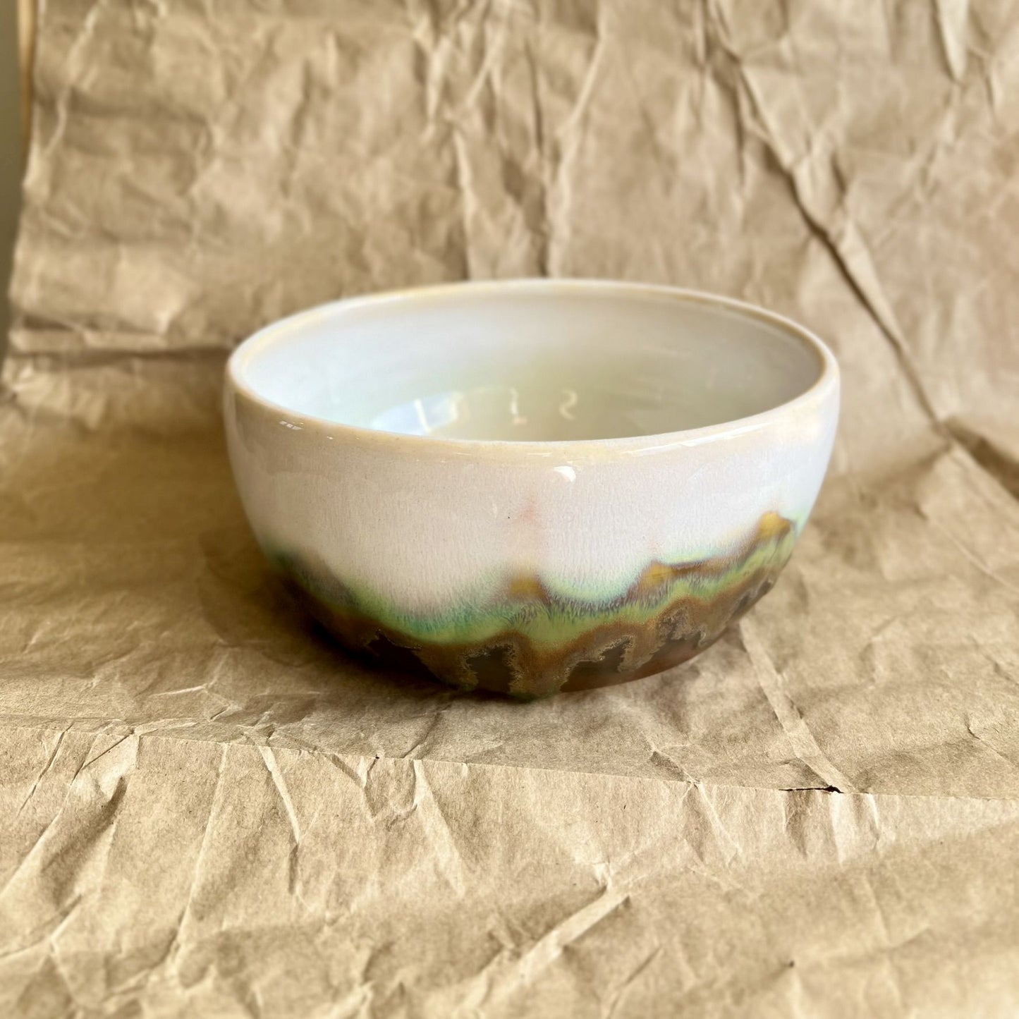 White ceramic bowl with green and walnut accent on a textured brown background