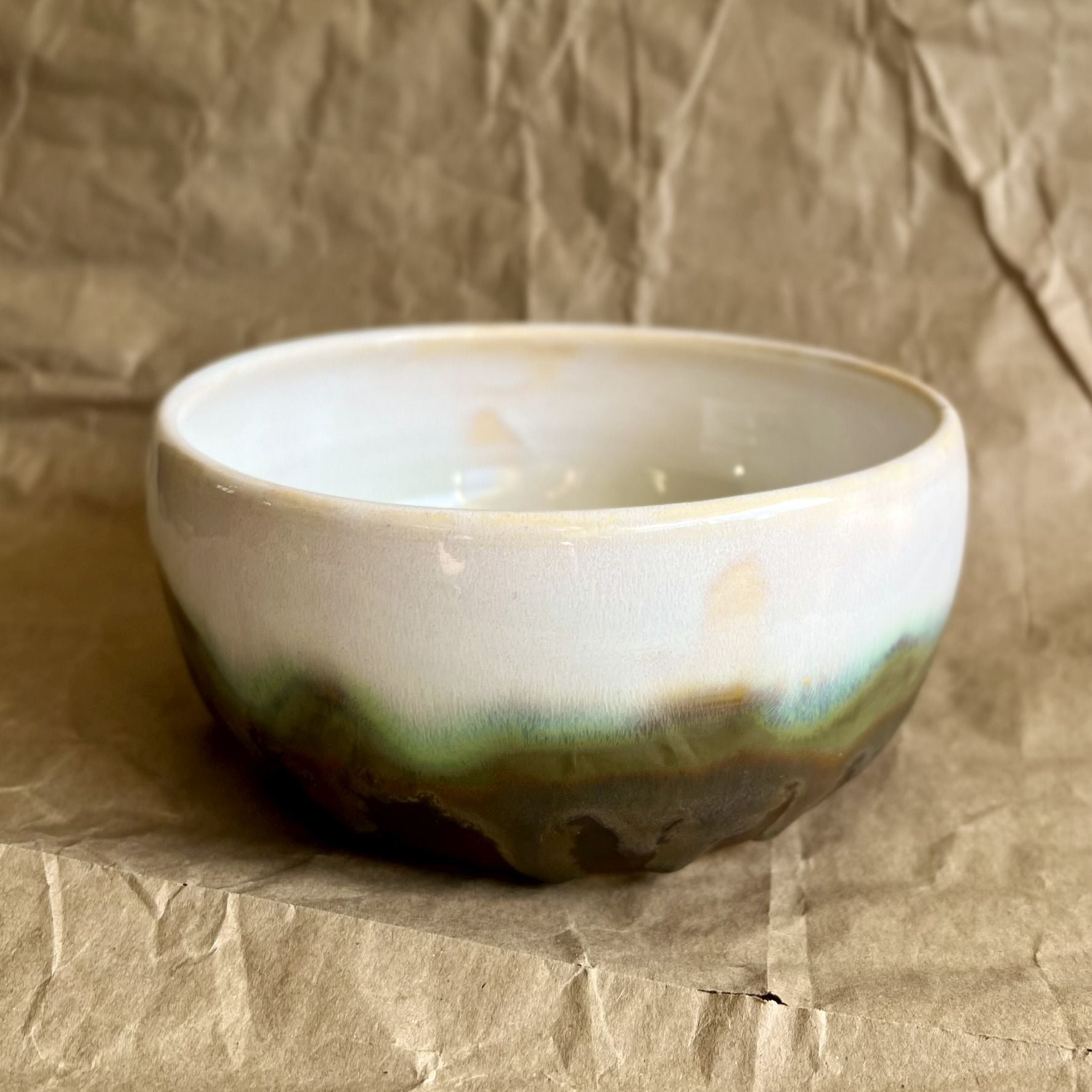 White ceramic bowl with green and walnut accent on a textured brown background