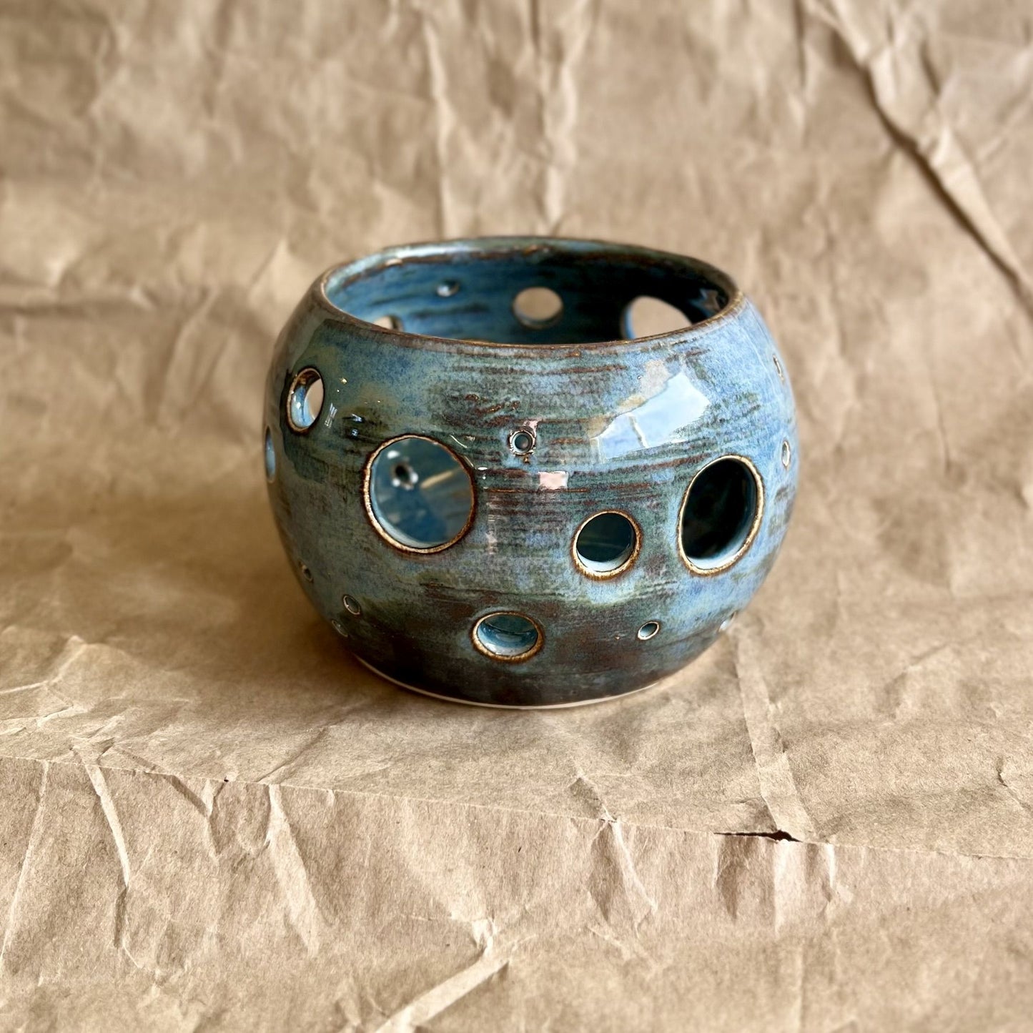 Blue ceramic votive with circular holes on a textured brown background