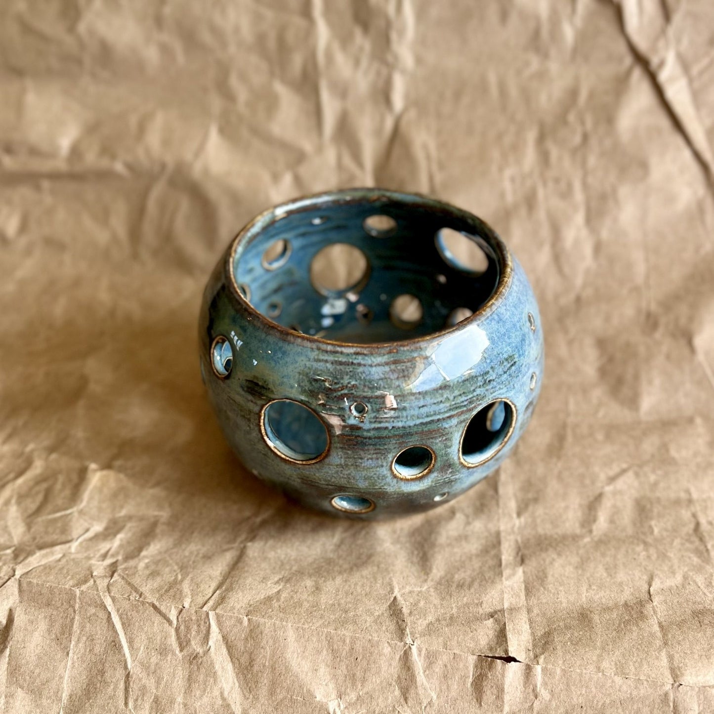 blue ceramic votive with circle cutouts on brown paper surface