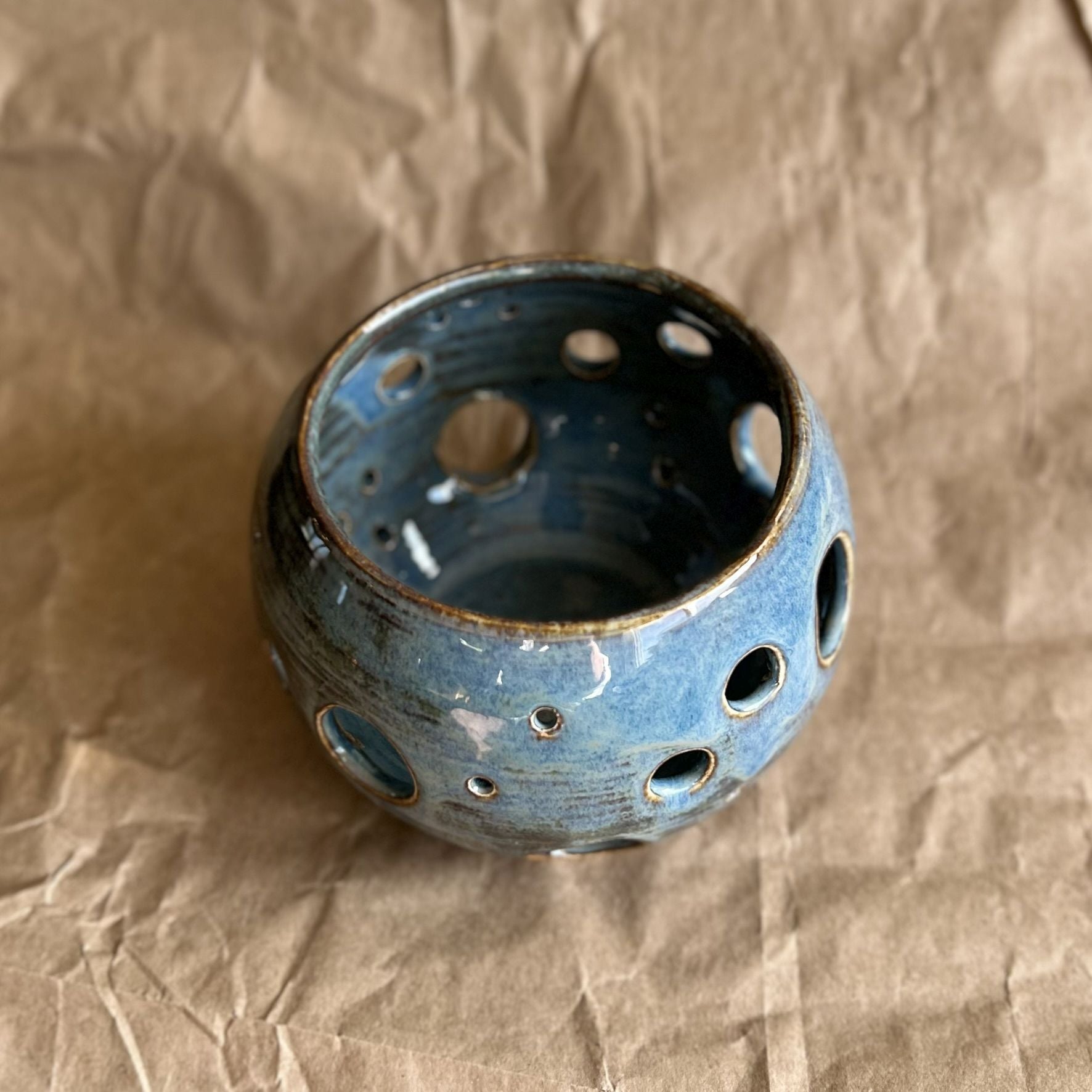 blue ceramic votive with circle cutouts on brown paper surface