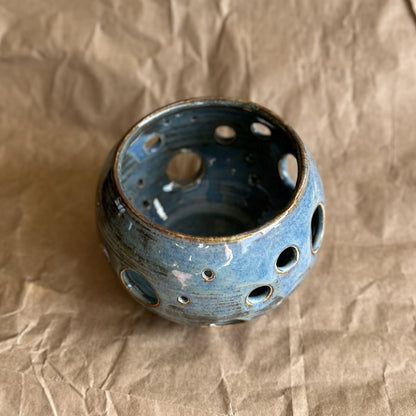 blue ceramic votive with circle cutouts on brown paper surface