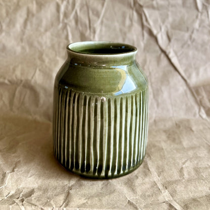 Tenmoku green ceramic jar vase with ribbed texture on a crumpled brown paper background