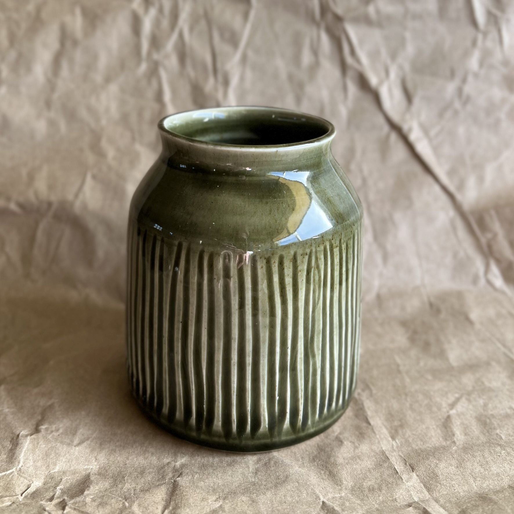 Tenmoku green ceramic jar vase with ribbed texture on a crumpled brown paper background