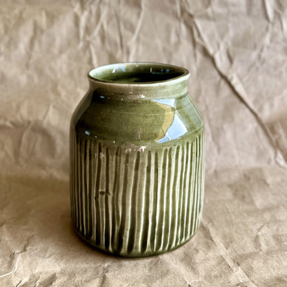 Tenmoku green ceramic jar vase with ribbed texture on a crumpled brown paper background