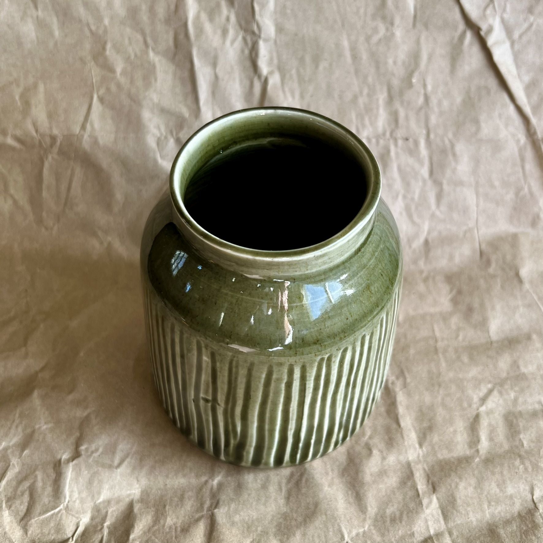 Tenmoku green ceramic jar vase with ribbed texture on a crumpled brown paper background