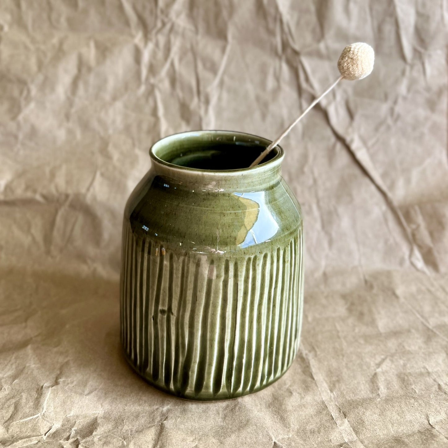 Tenmoku green ceramic jar vase with ribbed texture on a crumpled brown paper background