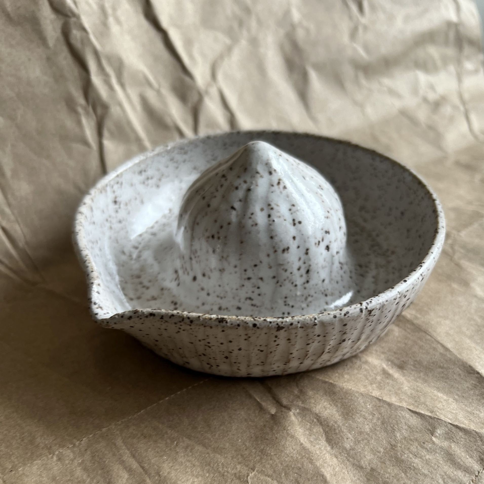 Speckled ceramic bowl with a white citrus press on a beige fabric background