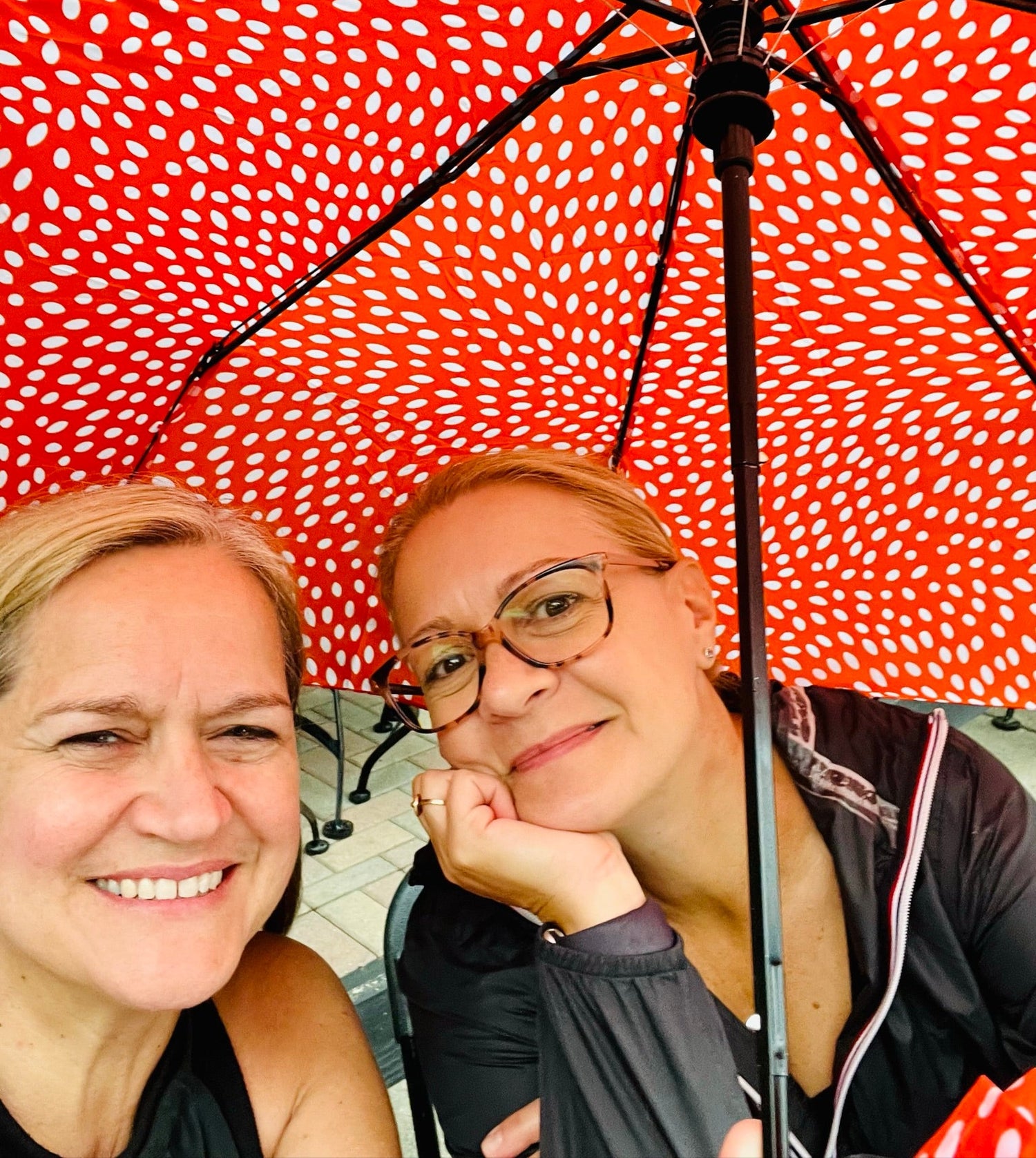 Two women standing under a red umbrella with white pattern