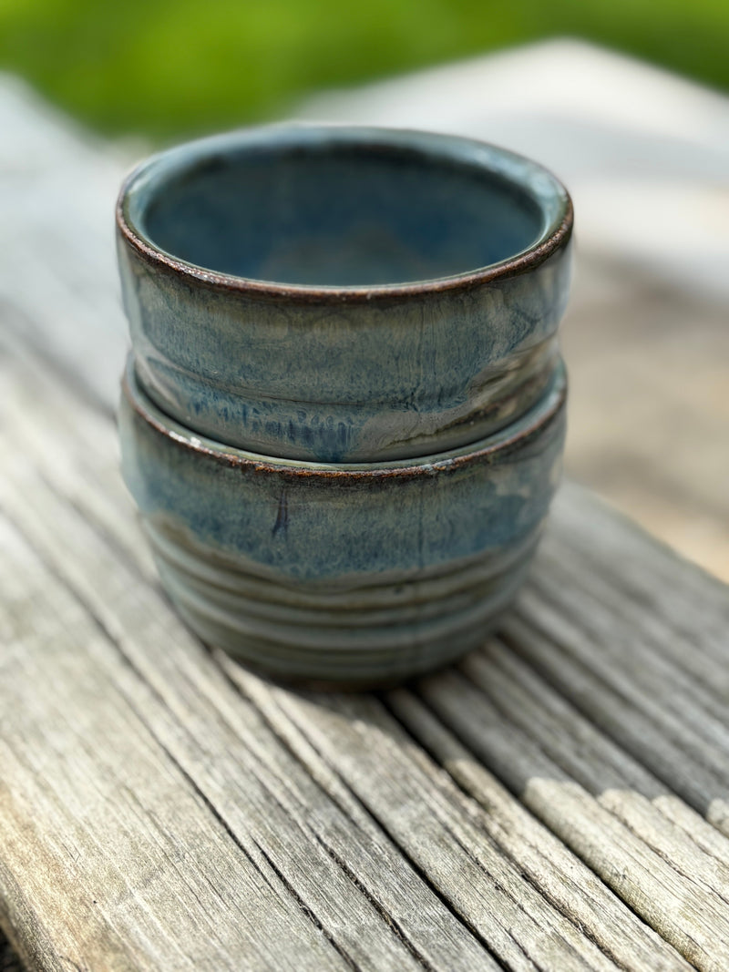 Stack of blue ceramic espresso cups on a wooden surface with a blurred green background