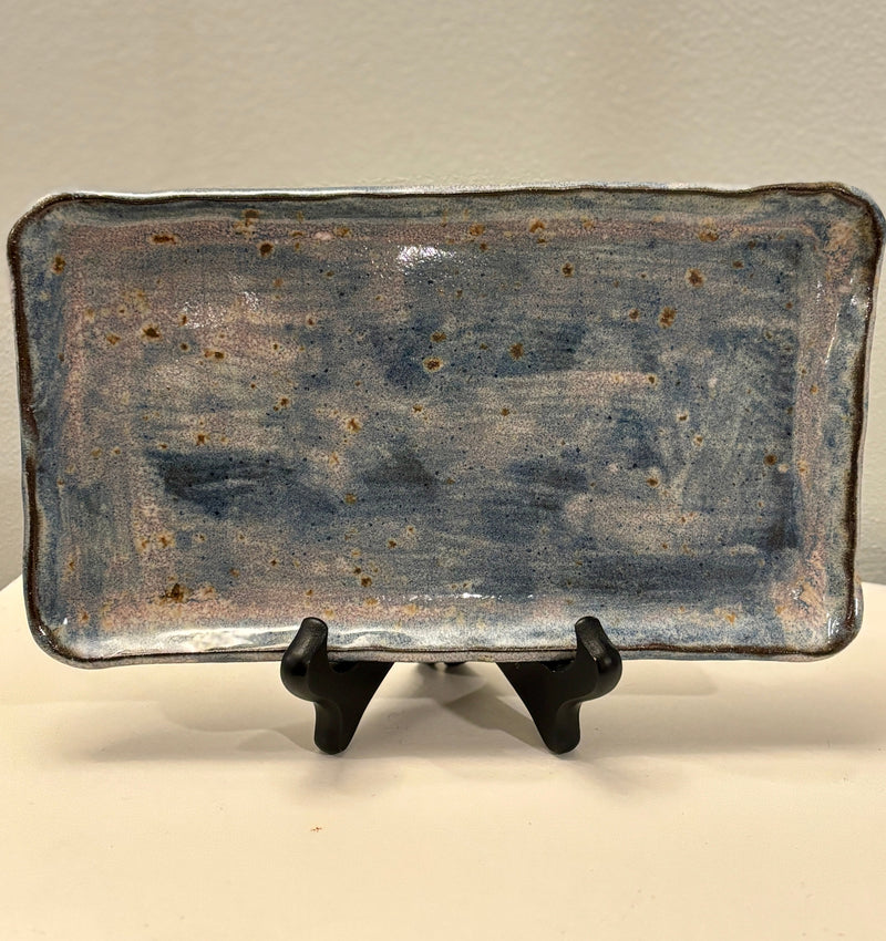 Rectangular ceramic tray with a textured surface on a stand against a neutral background