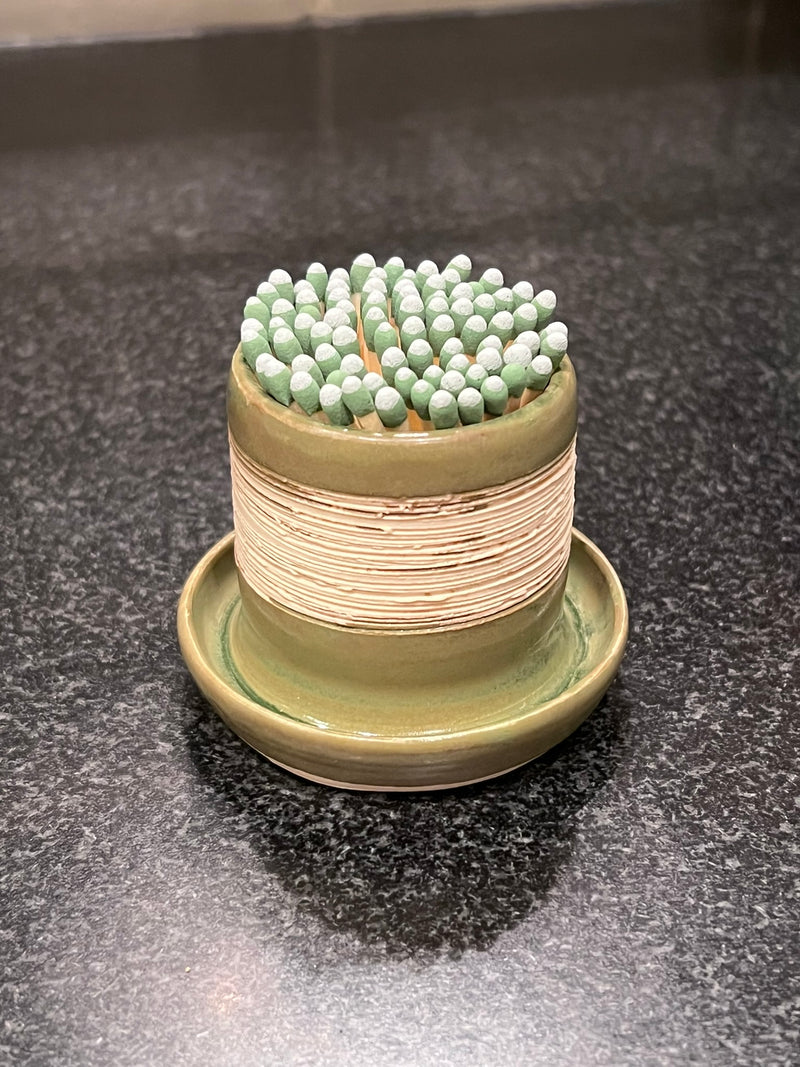 Ceramic container with green matches on a dark surface
